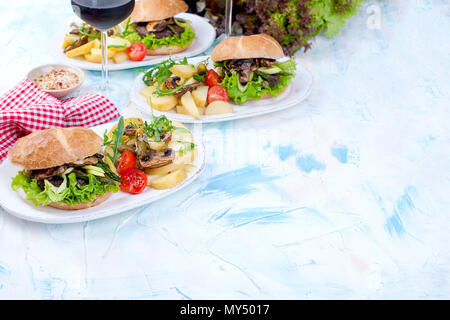 Deliziosi hamburger vegetariano e patate per tre. Insalata. Pranzo e vino. Sfondo di luce e spazio per il testo. La foto in orizzontale Foto Stock