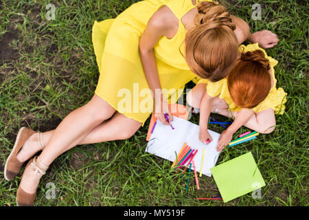 Vista aerea del redhead madre e figlia insieme di disegno durante la seduta di erba in posizione di parcheggio Foto Stock