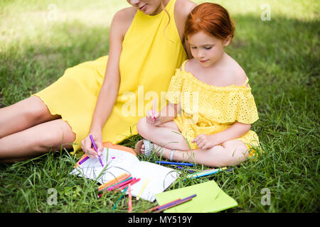 Ritagliato colpo di bella madre e figlia in abiti di colore giallo disegno insieme sull'erba Foto Stock