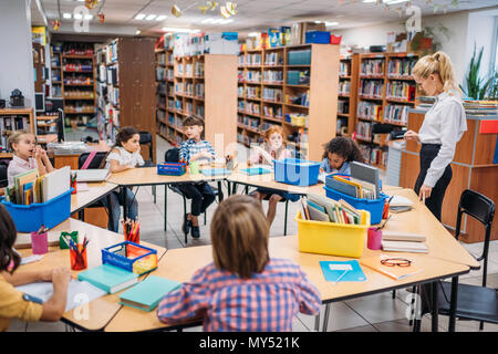 Bella giovane insegnante dando lezione per bambini in libreria Foto Stock