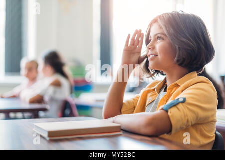 Adorable African American schoolgirl alzando la mano in classe Foto Stock