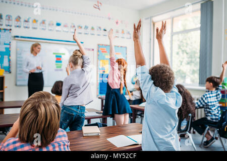 Kids alzando le mani in classe per rispondere alle domande degli insegnanti Foto Stock
