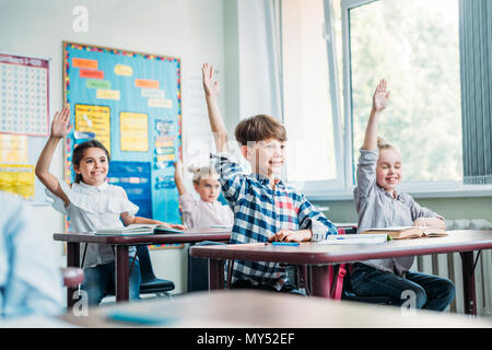 Felici i bambini piccoli, alzando le mani in classe Foto Stock