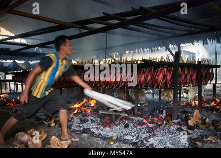 Un lavoratore sta mantenendo la distribuzione di buccia di cocco che brucia che ha usato come combustibile per fumare le carni di tonno di skipjack a Bitung, Sulawesi del Nord, Indonesia. Foto Stock