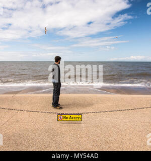 Blackpool, Inghilterra, Regno Unito - 1 Agosto 2015: Un uomo guarda al Blackpool Beach sea difese a alta marea, dietro a nessun segno di accesso, mentre i gabbiani volano overhe Foto Stock