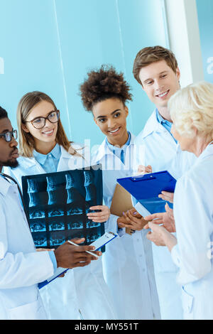 Un gruppo multirazziale di giovani stagisti di medici ad ascoltare un anziano medico in un corridoio di ospedale Foto Stock
