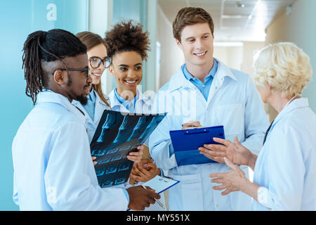Un gruppo multirazziale di giovani stagisti di medici ad ascoltare un anziano medico in un corridoio di ospedale Foto Stock