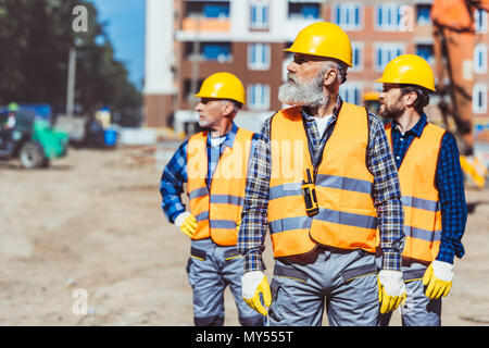 Lavoratori edili in giubbotti riflettenti e hardhats fuori, esaminando il sito in costruzione Foto Stock
