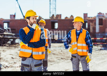 Lavoratori edili in uniforme in piedi fuori, esaminando il sito in costruzione Foto Stock