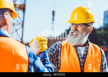 Sorridente operaio edile in uniforme di protezione si stringono la mano con un collega Foto Stock