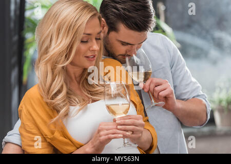 Abbracciando bella giovane bevendo vino insieme a casa Foto Stock