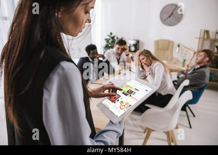 Giovane imprenditrice utilizzando tablet con il sito web di ebay sullo schermo mentre i colleghi una conversazione Foto Stock