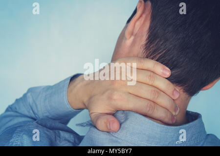 Close up di giovani man mano sul suo collo - dolore al collo concetto. una frattura delle vertebre cervicali. giovane trattiene la sua mano sul collo su un backg blu Foto Stock