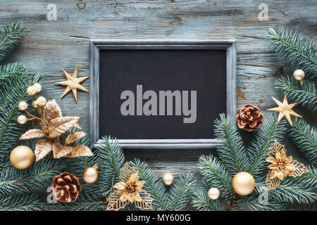 Verde e oro sullo sfondo di Natale. Decorate Abete rami attorno a Chalk board su legno rustico. Vista da sopra con copia spazio. Foto Stock