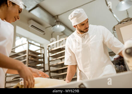 Giovani fiduciosi bakers lavora con impasto industriale rullo alla fabbricazione di cottura Foto Stock