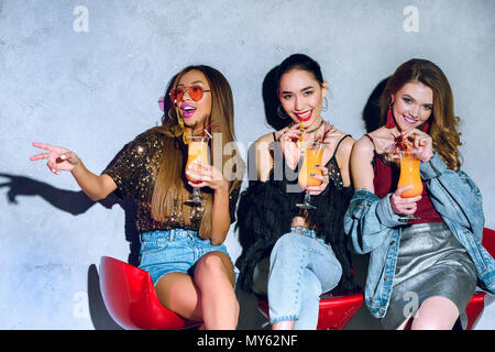 Felice elegante ragazze multietnica seduti su sgabelli da bar e di bere un cocktail a parte Foto Stock