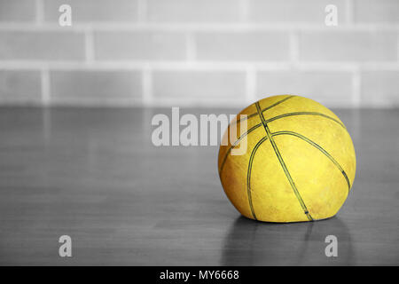 Vecchio stanco usurati piatto giallo sgonfiato basket chiuso sul pavimento in legno con sfondo mattone. Mancanza di prestazioni di lustre. Bianco e nero co isolato Foto Stock