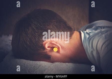 Giovane ragazzo bello è addormentato sul lettino vestita di nero t-shirt. Close up ritratto. Giornata di riposo, Siesta. gialla tappi auricolari nelle orecchie degli uomini. salvezza f Foto Stock