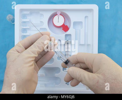 Una destrorsa anestesista tenendo una siringa di lidocaina o novocaine in preparazione per la somministrazione di un anestetico spinale. Foto Stock