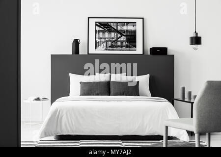 Poster su nero testata del letto bianco in contrasto interiore camera da letto grigio con sedia e lampada Foto Stock