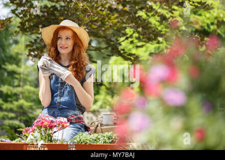 Giovane donna in appoggio e decollare la sua guanti dopo il giardinaggio nel suo cortile Foto Stock
