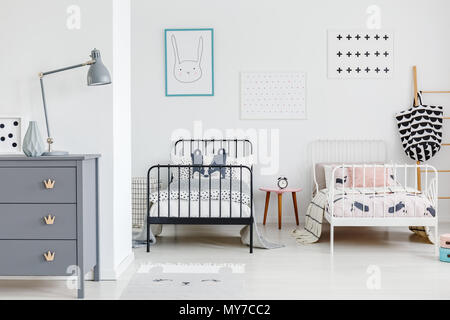 La Lampada sul cabinet grigio in una luminosa camera da letto per bambini con interni in bianco e nero sotto il letto poster. Foto reale Foto Stock