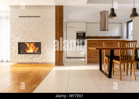 Camino nella spaziosa casa bianca interno con sedie di legno al tavolo vicino alla cucina. Foto reale Foto Stock