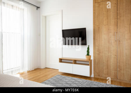 Armadio in legno accanto alla televisione sul muro bianco in hotel interiore camera da letto con la porta. Foto reale Foto Stock