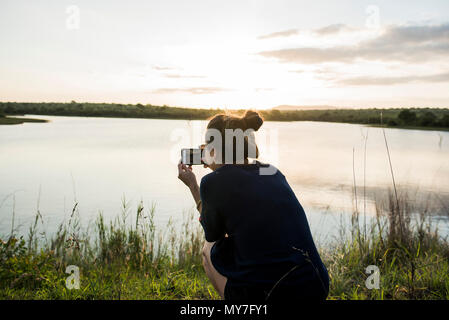 Giovane turista femminile fotografare fiume nel Parco Nazionale di Kruger, Sud Africa Foto Stock