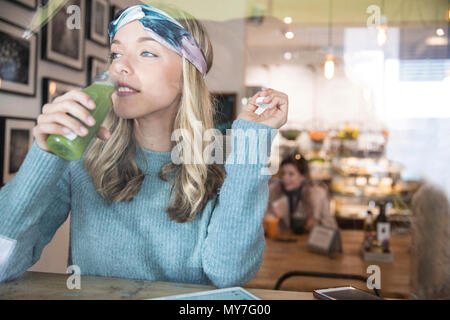 Giovane donna di bere succo di verdura al cafe finestrino Foto Stock
