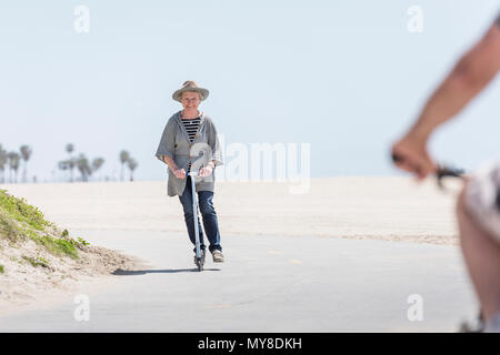 Senior di equitazione donna scooter push sulla spiaggia Foto Stock