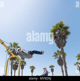 Senior donna su swing, marito in carrozzella Foto Stock