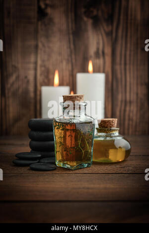 Vintage bottiglia con olio masssage, candele e pietre per massaggio stone su sfondo di legno Foto Stock