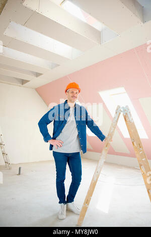 A piena lunghezza shot di sorridere lavoratore edile in piedi sulla scaletta mentre guarda la fotocamera e sorridente. Foto Stock