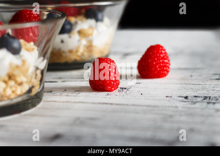 Lamponi Mirtilli, cereali e yogurt in una ciotola di vetro su assicelle di legno. Una sana colazione per una vita sana. L'immagine orizzontale. Foto Stock