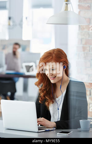 Lavoratore di ufficio utilizzando laptop e ascoltare musica mentre lavora Foto Stock