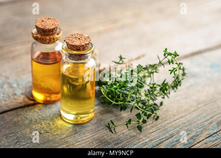 Olio essenziale di timo in un flacone di vetro con tappo di sughero e di timo fresco herb su sfondo di legno Foto Stock