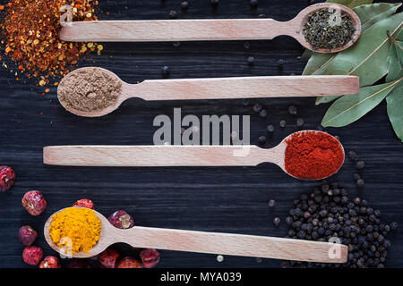 Quattro cucchiai di legno con varie spezie scuro su sfondo di legno Foto Stock