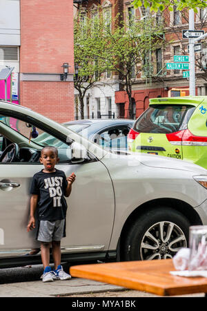 Ragazzo che indossa un 'Just Do It in piedi accanto a AUTO, tirando il viso, Harlem, New York City, Stati Uniti d'America Foto Stock