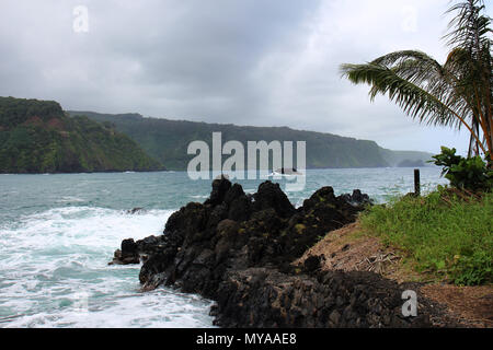 Tourquoise acqua dall'Oceano Pacifico che fluisce in una roccia lavica cove foderato con scogliere riempito con vegetazione lussureggiante in background a Lookou Wailua Foto Stock