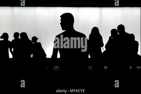 Silhouette di un giovane uomo in piedi da sola e una folla di gente che camminava sfocato dietro di lui nella notte Foto Stock