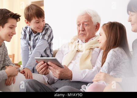 Dei bambini felici guardando loro sorpreso il nonno tenendo un tablet Foto Stock