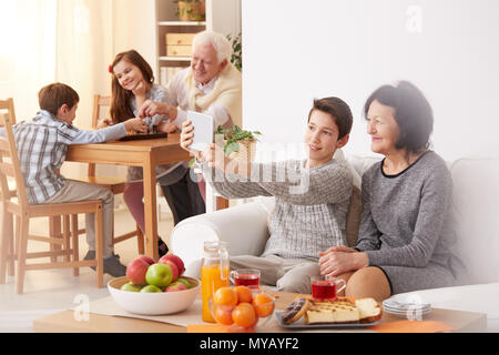 Nipote di prendere una selfie sorridente con la nonna e il nonno a giocare a scacchi con i nipoti Foto Stock