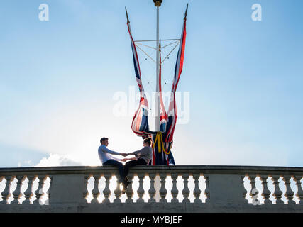 Coppia giovane seduto sul muro, tenendo le mani, accanto a British flag in St James Park, Londra, Inghilterra, Regno Unito Foto Stock