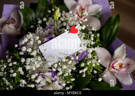 Schermata bianca vuota biglietto di auguri con il bianco bouquet di fiori e piccoli cuore rosso .vista dall'alto. mock up.elegante mockup branding per visualizzare le tue opere.orchidee e lisianthuses. Giorno speciale, evento invatation. Foto Stock