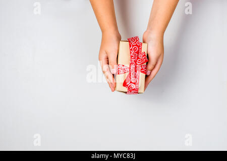 Childs mani dono in bianco imballaggio con nastro rosso su sfondo bianco, vista dall'alto. Concetto di vacanza. Copia dello spazio. Foto Stock