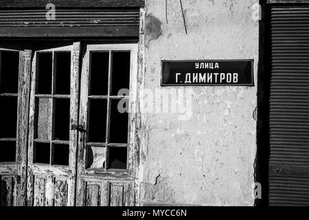 Street latta sign in cirillico G.Dimitrov su abbandonato casa in rovina nel piccolo villaggio bulgaro, immagine in bianco e nero Foto Stock