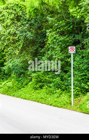 Piccole no-simbolo di parcheggio sul bordo del vuoto strada asfaltata contro fitti cespugli. Foto Stock