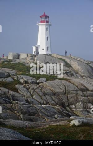 Peggy's Cove, Nova Scotia, Canada: Visitatori tour il pittoresco Peggy's Point Lighthouse (1914) è avvolta nella nebbia di mattina. Foto Stock