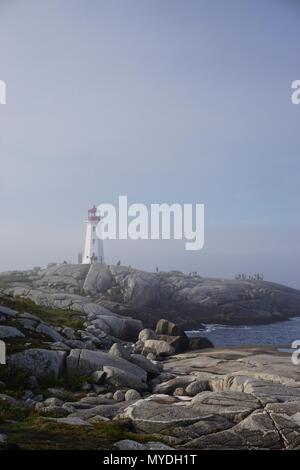 Peggy's Cove, Nova Scotia, Canada: Peggy's Point Lighthouse (1914) è avvolta nella nebbia di mattina con le onde che si infrangono sulla costa rocciosa. Foto Stock